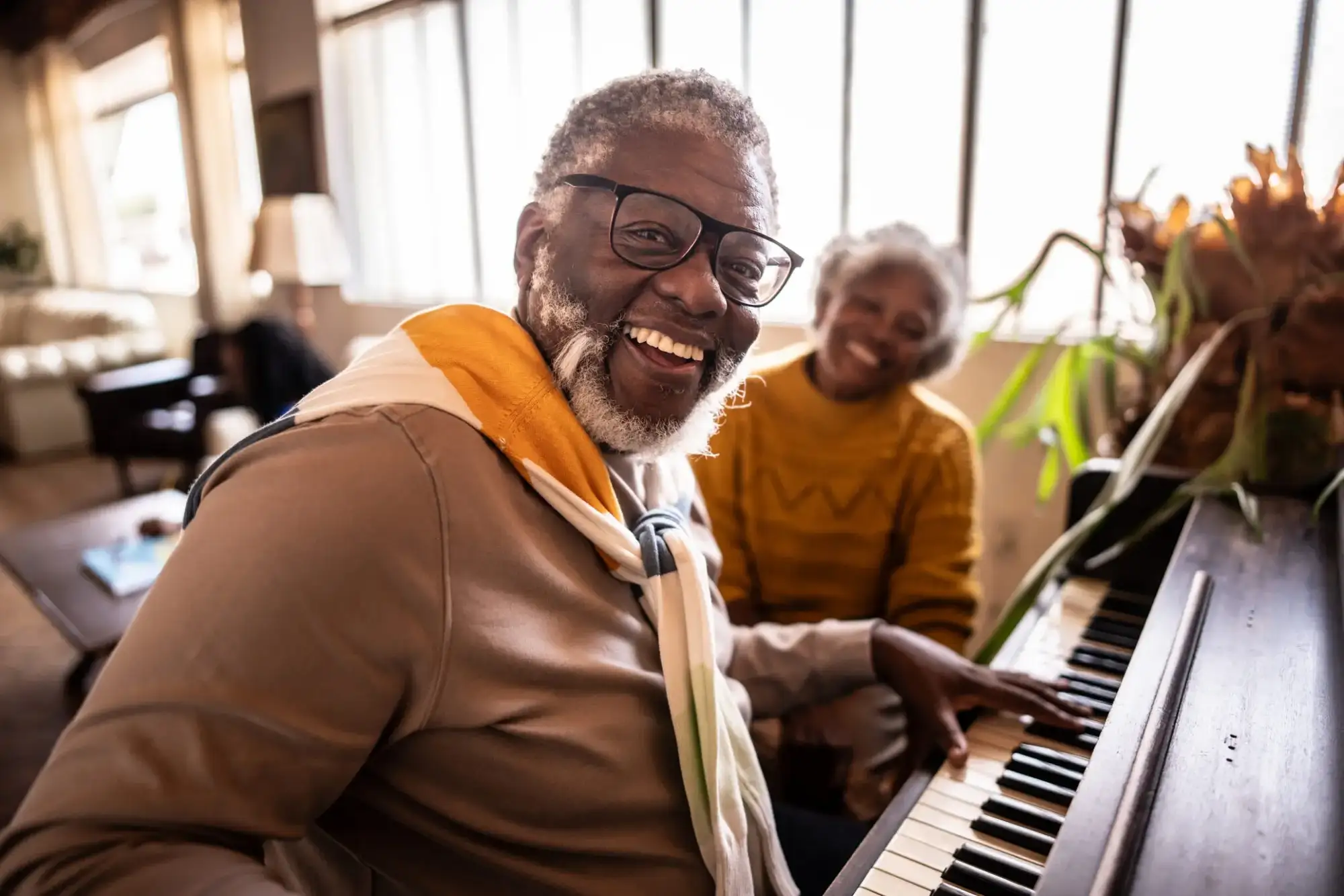 culturally-curious-at-stoneridge-blog-1 Senior man playing piano next to senior woman. The are exploring culturally curious events at StoneRidge.